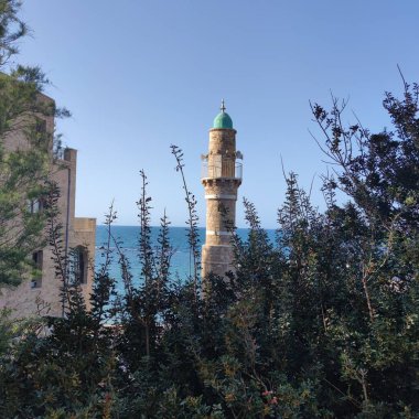 İsrail 'in Eski Jaffa, Tel Aviv-Yafo kentindeki Al-Bahr Camii minaresinin manzarası. Arka planda Akdeniz ve önde yemyeşil alanlar var..