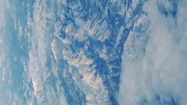 Yumuşak kabarık bulutların üzerinde uçan kanatlar ve yolcu tarafından lomboz delikten görülen karlı dağlar. Dikey görünüm. Yüksek kalite 4k görüntü