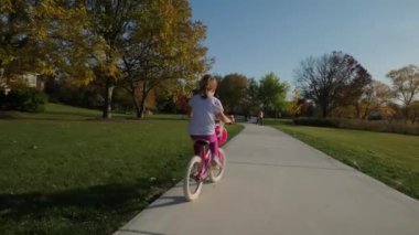 Anne ve kızı güneşli bir günde bir parkta ve banliyö caddesinde bisiklet sürerler. Yüksek kalite 4k görüntü