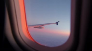 Wing of flying above soft fluffy clouds airplane as seen by passenger through porthole. High quality 4k footage