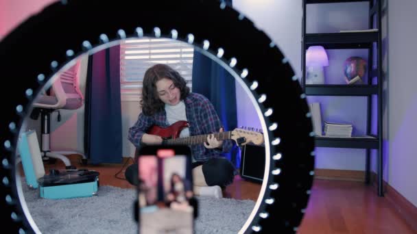 アート ウーマン ブロガー オンラインレッスン録音 ギター演奏 携帯電話を使用して座っている間陽気な女性ブロガーはギターを演奏します 高品質4K映像 — ストック動画