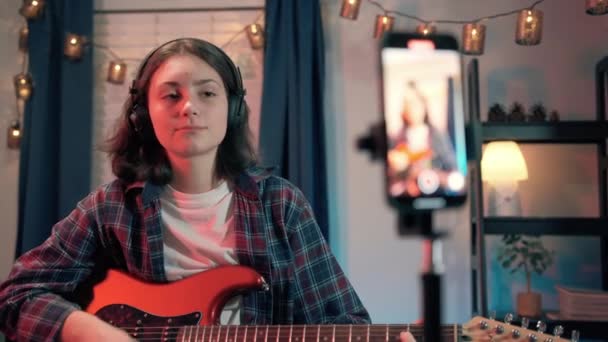 艺术女性博客 在线课程记录 弹吉他 快乐的女性博主坐在手机上弹奏吉他 高质量的4K镜头 — 图库视频影像
