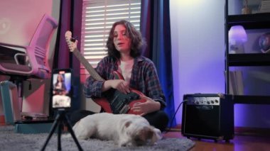 Bir köpekle otururken gitar çalan neşeli bir genç kadın. Yüksek kalite 4k görüntü