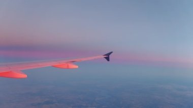 Wing of flying above soft fluffy clouds airplane as seen by passenger through porthole. High quality 4k footage