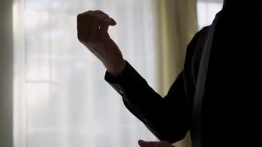 Silhouette of a man putting on his jacket in dark room on the background of the window. High quality 4k footage