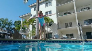 The little girl jumps into the pool. A view of joyful leisure of jumping little girl into a swimming pool. High quality 4k footage
