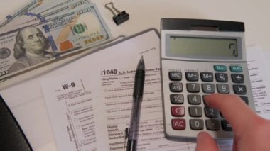 calculate the amount on a calculator 1040 and W9 individual tax form are placed on desk of American citizen. High quality 4k footage