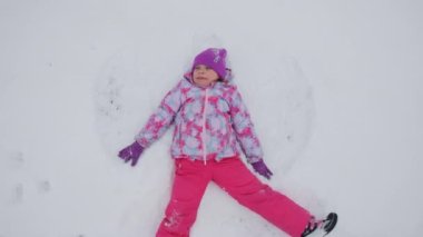 Happy little girl lying on a snow and shows angel, slow motion. High quality 4k footage