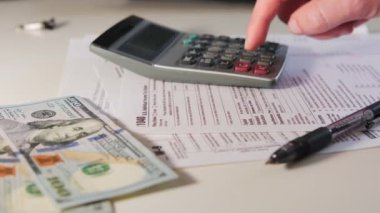calculate the amount on a calculator 1040 and W9 individual tax form are placed on desk of American citizen. High quality 4k footage