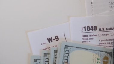 An American dollar tax bill, pen calculator and U.S. money. 1040 and W9 individual tax form are placed on desk of American citizen. High quality 4k footage