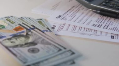 An American dollar tax bill, pen calculator and U.S. money. 1040 and W9 individual tax form are placed on desk of American citizen. High quality 4k footage