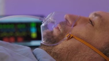 Side view of mature Caucasian man wearing oxygen mask, lying in bed in room of clinic,. High quality 4k footage