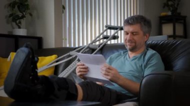 Kırık bacağı olan mutlu bir adam elinde bir sigorta sözleşmesi tutuyor, para üstüne yağıyor. Yüksek kalite 4k görüntü