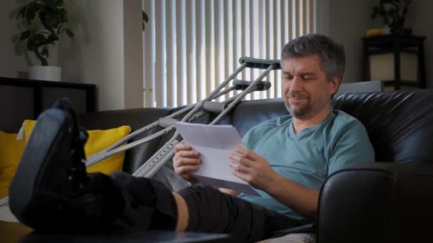 足の骨折した幸せな男が手に保険契約を結んでいる お金が彼に落ちている 高品質4K映像 — ストック動画