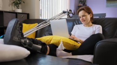 A happy woman with a broken leg is working on a laptop. High quality 4k footage