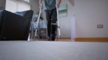A man with broken leg in black Fracture Boot cast trying to walk with crutches in living-room. . High quality 4k footage