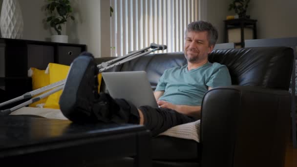 Hombre Feliz Con Una Pierna Rota Está Trabajando Portátil Imágenes — Vídeo de stock