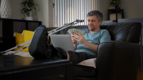 足が折れた幸せな男がノートパソコンで働いている 高品質4K映像 — ストック動画