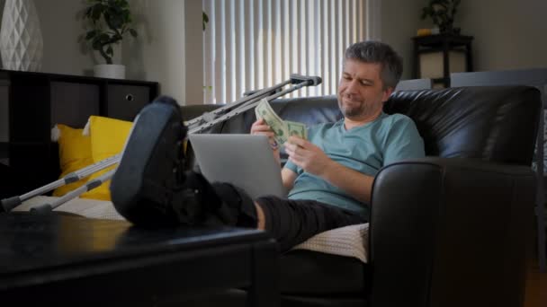 足が折れた幸せな男がノートパソコンで働いている 高品質4K映像 — ストック動画