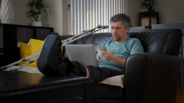 足が折れているタイヤードの男がノートパソコンで働いている 高品質4K映像 — ストック動画