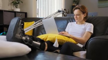 Kırık bacaklı mutlu bir kadın dizüstü bilgisayarda çalışır. Geniş açı. Yüksek kalite 4k görüntü