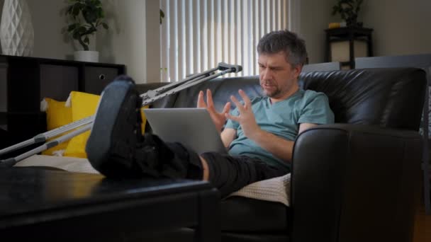 一个腿断了的疲倦男人正在笔记本电脑上工作 高质量的4K镜头 — 图库视频影像