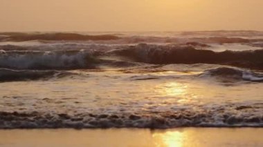 Okyanus dalgası gün doğumunda kıyıda kırılır. Ağır çekim. Yüksek kalite 4k görüntü