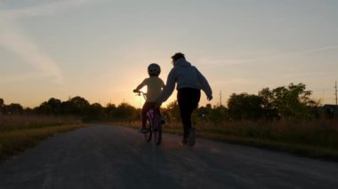 Annesi kızına bisiklet sürmeyi öğretiyor. Mutlu aile çocukluğu hayali ebeveyn ve küçük çocuklar parkta bisiklet silueti sürmeyi öğrenirler. Yüksek kalite 4k görüntü