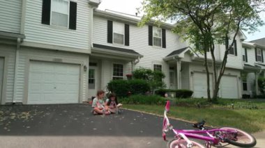 İki kız bisikletin yanında evin yanında oturuyorlar. Kamerayı çek. Yüksek kalite 4k görüntü