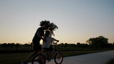 Babası kızına bisiklet sürmeyi öğretiyor. Mutlu aile çocukluğu hayali, parkta bisiklet silueti sürmeyi öğrenmek. Yüksek kalite 4k görüntü