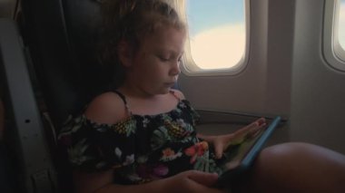 Küçük bir kız uçakta oturur, tabletle oynar ve kapı deliğinden bakar. Yüksek kalite 4k görüntü