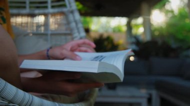 Bir kadın, sallanan sandalyede oturmuş, tatilde kitap okuyor. Kapatın. Yüksek kalite 4k görüntü