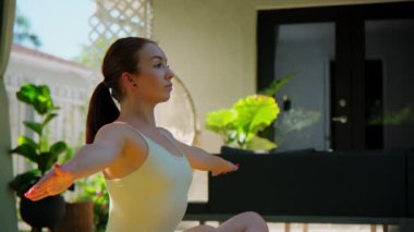 Spor kıyafetli bir kadın, güzel bir tropik bahçe bahçesinde yoga yaparken mindere oturmuş poz veriyor. Kapatın. Yüksek kalite 4k görüntü