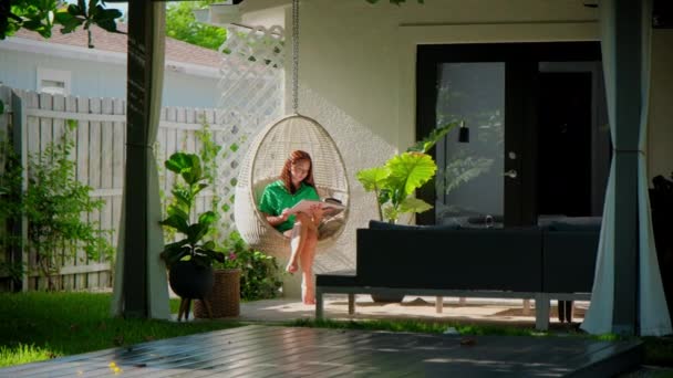 女性は休暇中に本を読み 熱帯の裏庭にロッキングチェイに座っています カメラを移動する 高品質の4K映像 — ストック動画