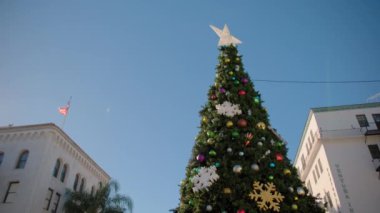 Santa Barbara, Kaliforniya 'daki Noel ağacı, güneşli bir günde palmiye ağaçları ve Amerikan bayrağının arka planına karşı. Geniş açı. Yüksek kalite 4k görüntü