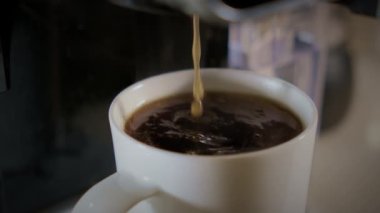Makineden beyaz fincana dökülen koyu kahvenin yavaş hareketi. Ev ya da ofis mutfağında yeni bir kafe. Kapatın. Yüksek kalite 4k görüntü