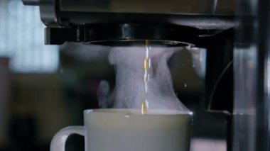 Sıcak kahvenin yavaşça makineden beyaz fincana dökülmesi. Ev ya da ofis mutfağında yeni bir kafe. Kapatın. Yüksek kalite 4k görüntü