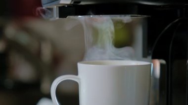 Makineden beyaz fincana dökülen sıcak siyah kahvenin yan görüntüsü. Evin mutfağında yeni bir kafe. Yüksek kalite 4k görüntü
