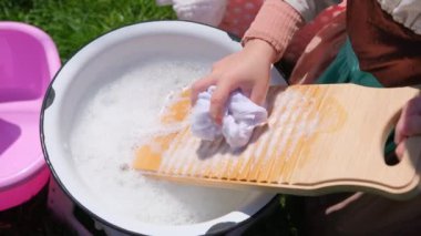 Eski moda çamaşır yıkama tahtasıyla dışarıda çamaşır yıkıyorum. Genç kadın eski bir çamaşır tahtasında yıkanıyor. Görüntüleri kapat. Yüksek kalite 4k görüntü