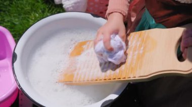 Eski moda çamaşır yıkama tahtasıyla dışarıda çamaşır yıkıyorum. Genç kadın eski bir çamaşır tahtasında yıkanıyor. Çekimi kapat. Yüksek kalite 4k görüntü