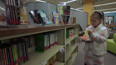 Okul kütüphanesindeki küçük kız bir kitap seçiyor. Naperville lL 'de. ABD 10 Mayıs 2024. Yüksek kalite 4k görüntü