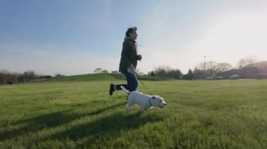 Parkta köpeğiyle koşan bir kadın. Gün batımında geniş bir görüntü. Ağır çekim. Yüksek kalite 4k görüntü