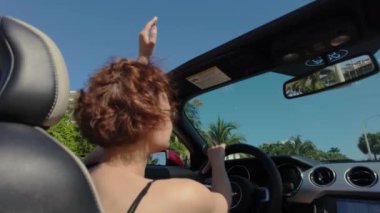 Cabriolet araba kullanan bir kadın, gün batımında el sallayan bir kadın. Dikiz aynası. Yüksek kalite 4k görüntü
