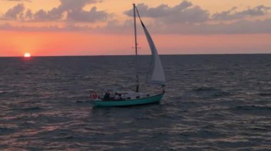 Bir yelkenlinin gün batımında derin sularda yelken açtığı sinematik geniş görüntü. Yüksek kalite 4k görüntü