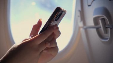 Genç bir kadın uçakta oturuyor ve telefonu tutuyor. Kapatın. Yüksek kalite 4k görüntü