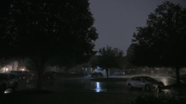 Geceleri banliyödeki ağaçların arasından şimşeklerin çaktığını gösteren geniş bir görüntü. Yüksek kalite 4k görüntü