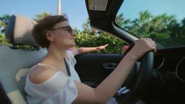 Mutlu kadın gün batımında el sallayarak Cabriolet araba kullanıyor. Yan görüntü görüntüsü. Yüksek kalite 4k görüntü
