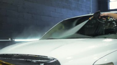 Araba yıkama makinesi, arabanın ön tarafını su basıncıyla yıkıyor. Profesyonel Araç Vücut Detaylı Atölyesi. Manzarayı kapat. Yüksek kalite 4k görüntü