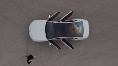 Beyaz bir arabanın üst görüntüsü tüm kapıları otomatik olarak açıyor ve bir kadın arabaya biniyor. Yüksek kalite 4k görüntü