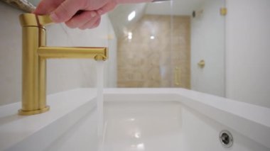 Adam elini açtı ve altın su musluğunu kapattı. Beyaz banyo. Banyodaki musluğu açıp kapamak. Görüntüleri kapat. Yüksek kalite 4k görüntü